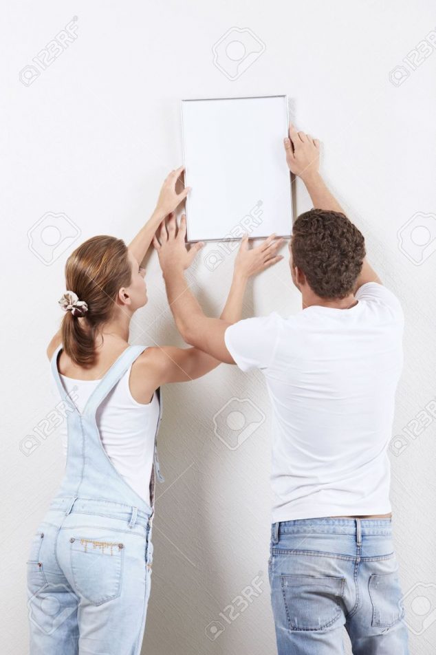 7952656 Young couple hanging up painting on the wall Stock Photo picture hang hanging 634x952 Useful Rules, Tips and Ideas About how High to Hang Pictures