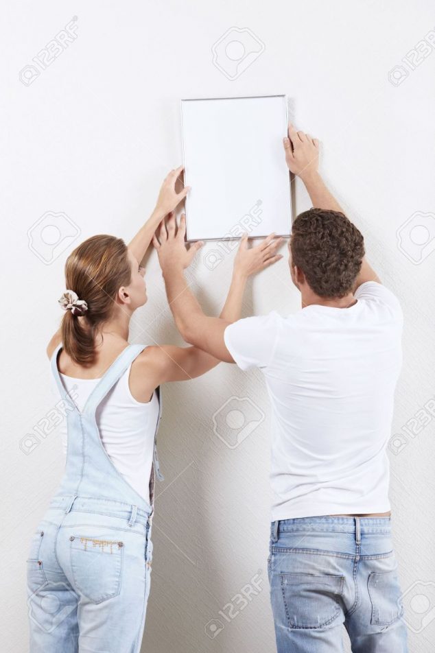 Useful Rules, Tips and Ideas About how High to Hang Pictures 7952656 Young couple hanging up painting on the wall Stock Photo picture hang hanging 634x952 Useful Rules, Tips and Ideas About how High to Hang Pictures